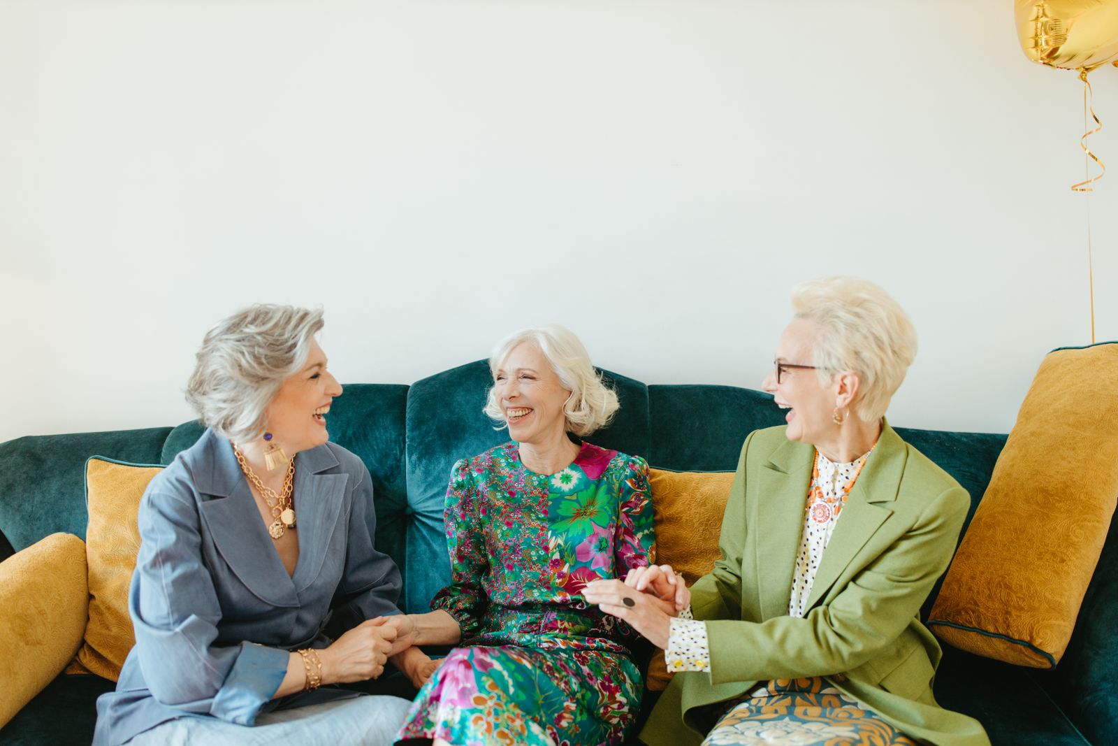 Three senior women laughing together on a couch in a bright living room